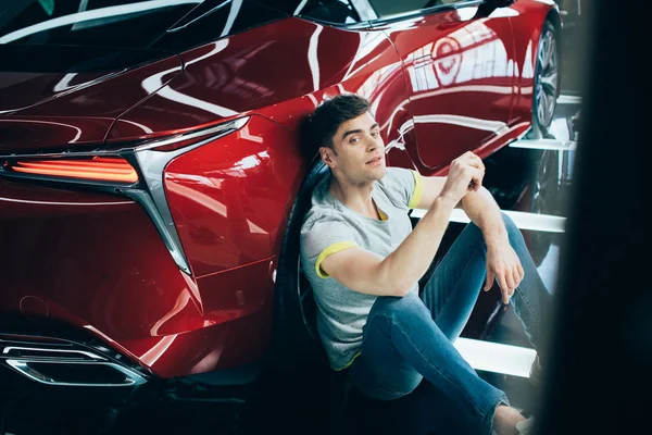 Selective focus of happy man sitting on floor near new car and looking at camera — Stock Photo