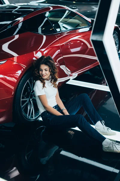 Selective focus of happy woman sitting on floor near new red car — Stock Photo
