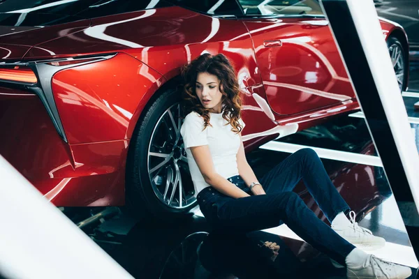 Selective focus of beautiful woman sitting on floor near new red car — Stock Photo