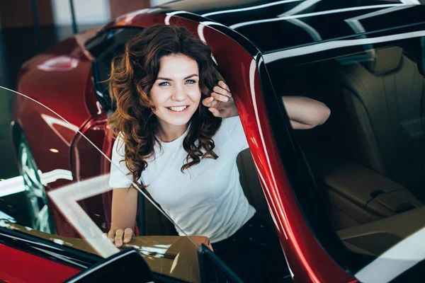 Messa a fuoco selettiva di donna felice seduta nella nuova auto rossa e guardando la fotocamera — Foto stock