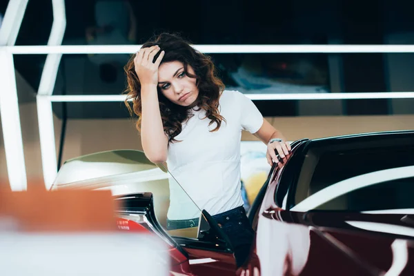 Selective focus of tired woman standing near car in car showroom — Stock Photo