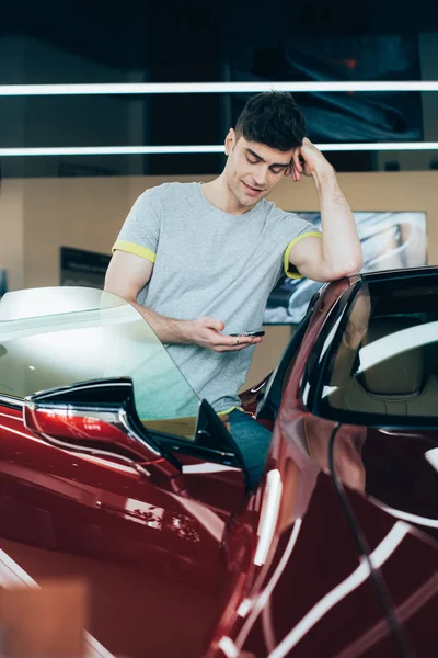 Selective focus of smiling man using smartphone while standing at car — Stock Photo
