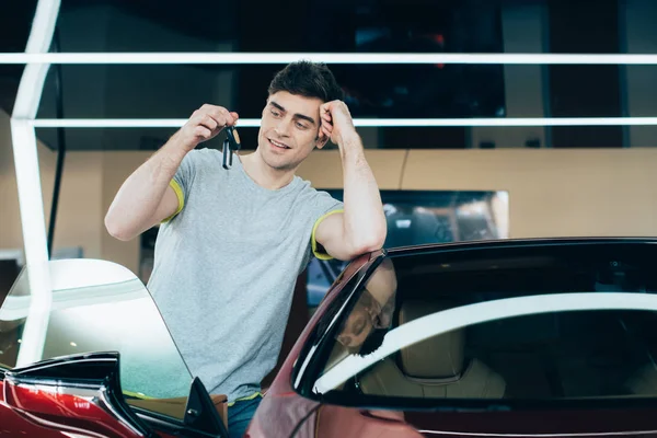 Foco seletivo de homem sorridente segurando chaves enquanto está perto de carro novo — Fotografia de Stock