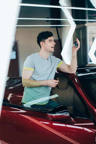 Selektiver Fokus des glücklichen Mannes, der Autoschlüssel hält, während er in der Nähe von Neuwagen steht — Stockfoto