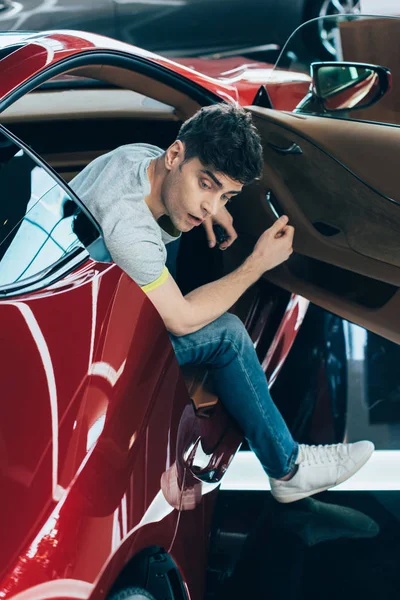 Selective focus of handsome surprised man sitting in new red car — Stock Photo