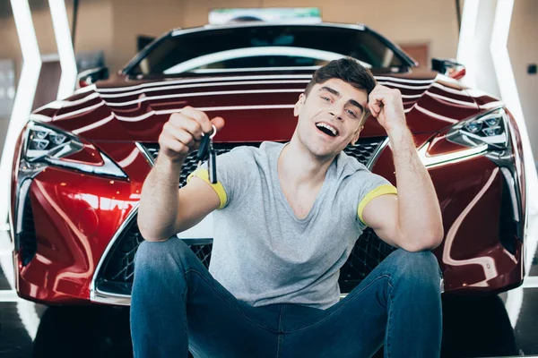 Foco seletivo de homem animado segurando chaves do carro enquanto sentado perto de novo carro vermelho — Fotografia de Stock