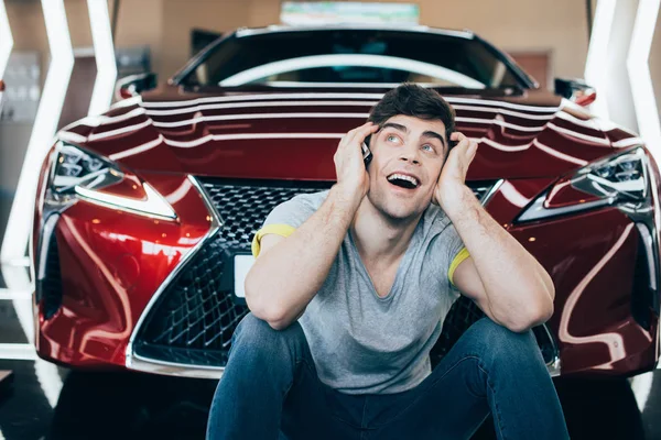 Selective focus of excited man sitting near new red luxurious car — Stock Photo