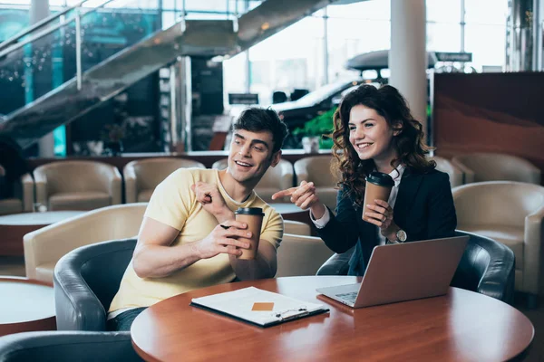 Smiling customer and car dealer sitting at table in car showroom and holding paper cups — Stock Photo