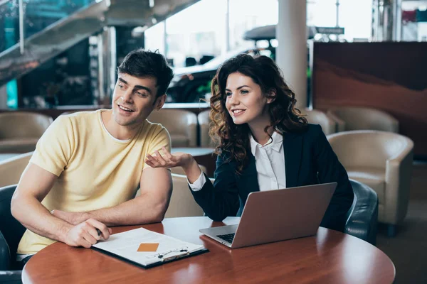 Rivenditore di auto sorridente e cliente seduto a tavola e guardando altrove — Foto stock