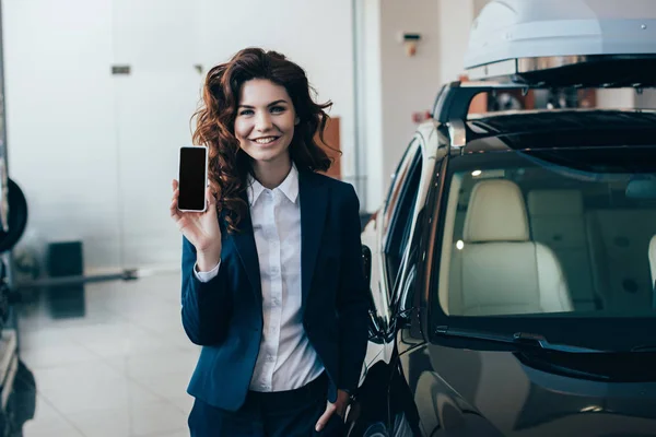 Красивая деловая женщина, стоящая с рукой в кармане и держа смартфон с чистым экраном — стоковое фото