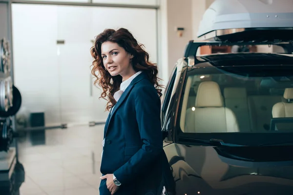 Beautiful businesswoman standing near car and holding hand in pocket — Stock Photo