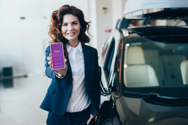 Foyer sélectif de souriante femme d'affaires tenant smartphone avec application instagram à l'écran — Photo de stock