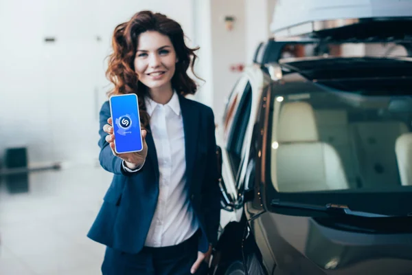 Избирательный фокус веселой деловой женщины, держащей смартфон с шазамом приложения на экране — стоковое фото