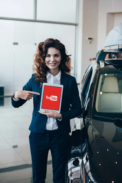 Mujer de negocios sonriente apuntando a la tableta digital con aplicación de youtube en la pantalla - foto de stock