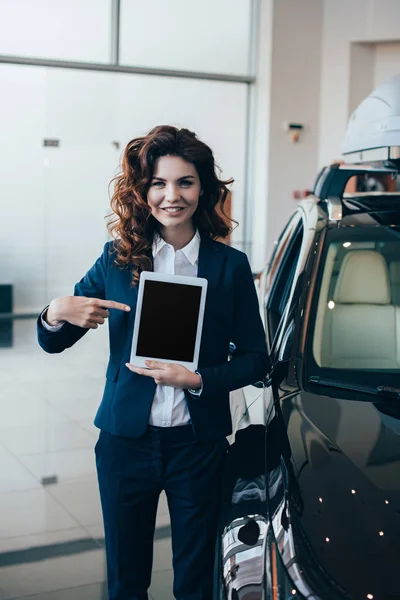 Mujer de negocios sonriente apuntando con el dedo a la tableta digital con pantalla en blanco - foto de stock