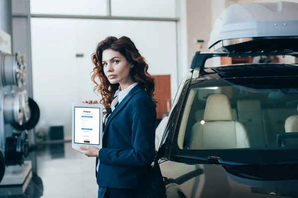 Mujer de negocios seria sosteniendo tableta digital con aplicación instagram en la pantalla - foto de stock