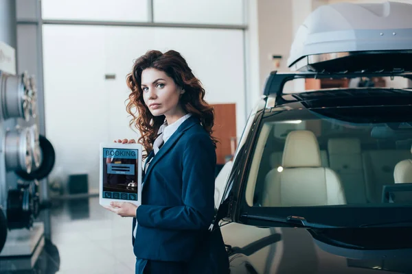 Serious businesswoman holding digital tablet with booking app on screen and looking at camera — Stock Photo