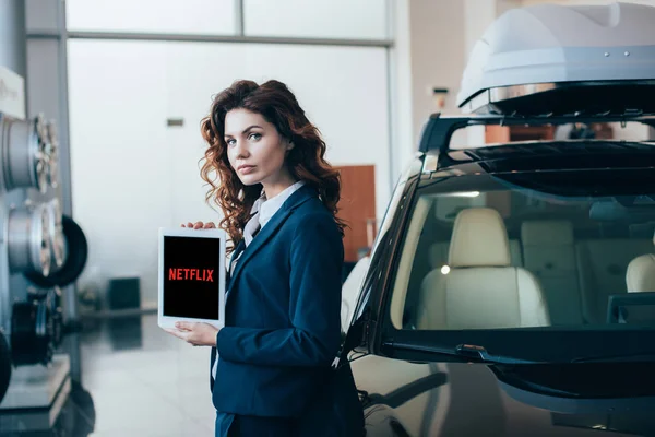 Atractiva empresaria sosteniendo tableta digital con aplicación de netflix en la pantalla y mirando a la cámara - foto de stock