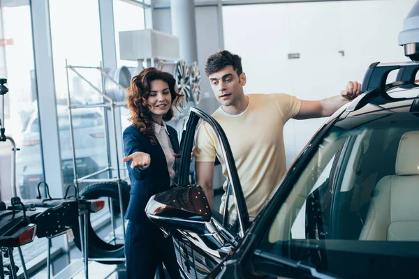 Selective focus of attractive car dealer and handsome man standing near new car — Stock Photo