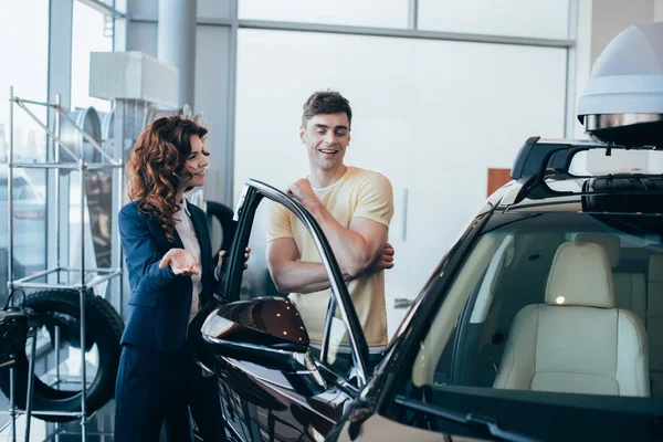 Selective focus of pretty car dealer and handsome customer standing near new car — Stock Photo