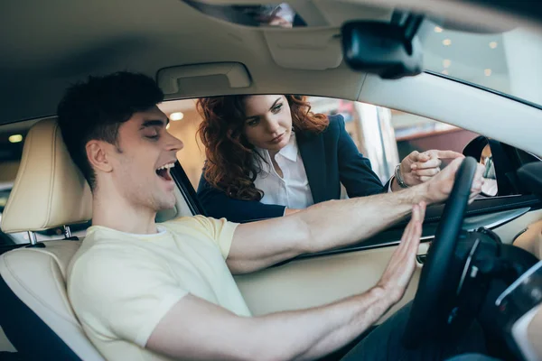 Aufgeregter Mann sitzt in Neuwagen neben Autohändler — Stockfoto