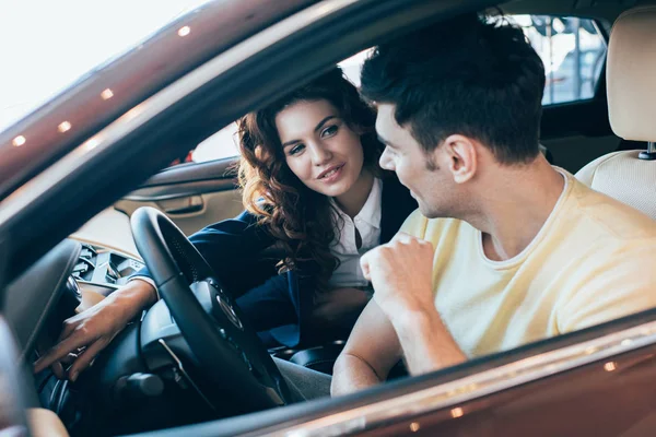 Enfoque selectivo de hombre guapo y distribuidor de coches bastante sentado en auto — Stock Photo