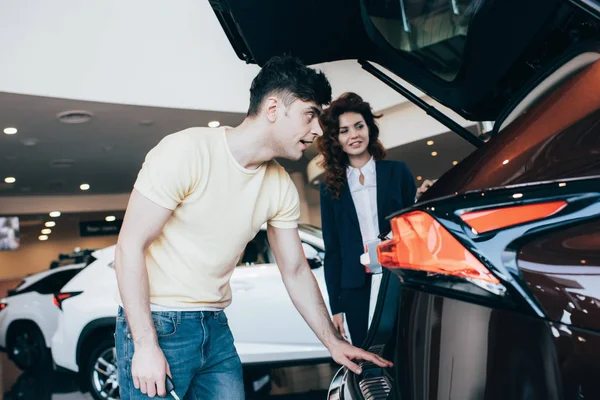 Selective focus of handsome man and attractive car dealer standing near new car — Stock Photo