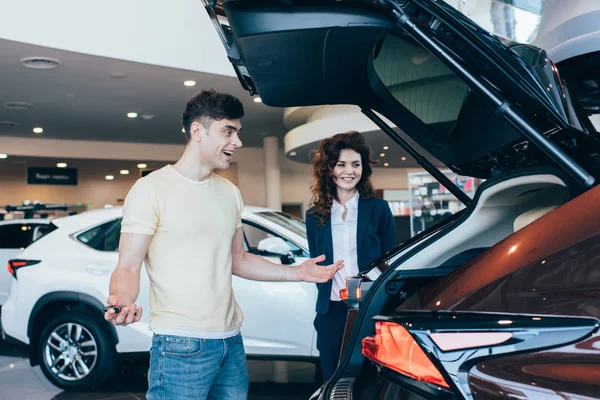 Selective focus of smiling car dealer and happy customer standing near new car — Stock Photo