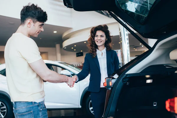 Веселый автомобильный дилер и клиент пожимает руку в автосалоне — стоковое фото