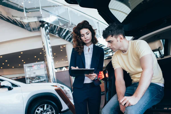 Handsome man looking at car dealer writing in clipboard — Stock Photo