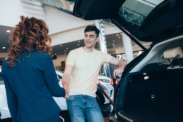 Foco seletivo de homem feliz e negociante de carro apertando as mãos no showroom do carro — Fotografia de Stock