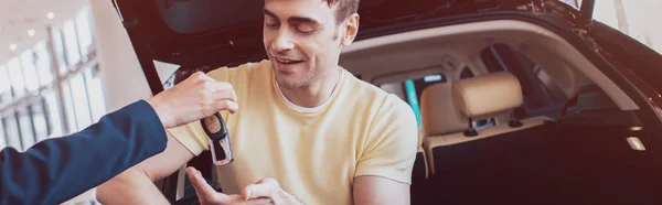 Tiro panorámico del hombre feliz tomando las llaves del coche del distribuidor del coche - foto de stock