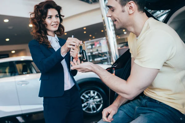 Selective focus of smiling car dealer giving car keys to happy client — Stock Photo