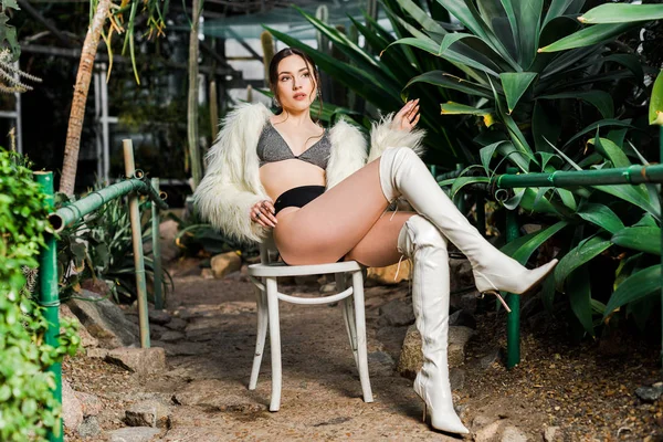 Relaxed sexy woman in faux fur coat and underwear sitting on chair in orangery — Stock Photo