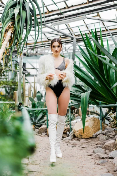 Full length view of sexy woman in faux fur coat and boots in orangery — Stock Photo