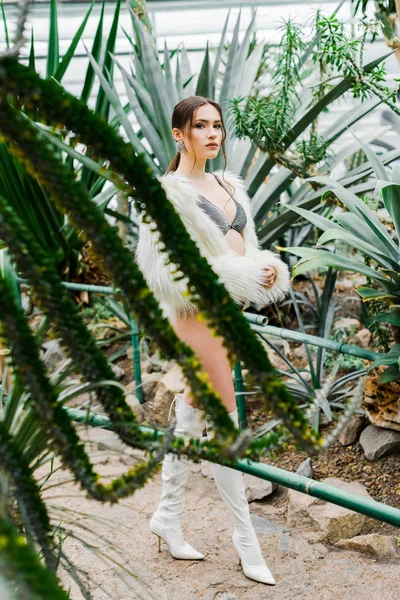 Full length view of sexy woman in faux fur coat and boots in orangery — Stock Photo