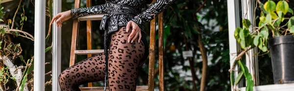 Foto panorámica de mujer sexy en pantimedias negras de pie cerca de escalera de madera en naranja - foto de stock