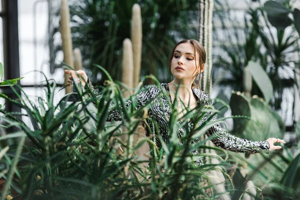 Attraktive nachdenkliche junge Frau gießt grüne Pflanzen in der Orangerie — Stockfoto