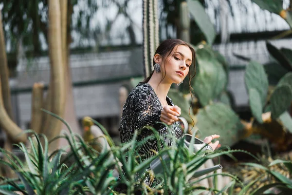 Atraente pensivo jovem mulher regando plantas verdes em orangery — Fotografia de Stock