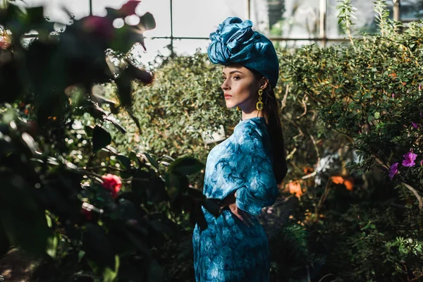 Preciosa joven en vestido azul y turbante en naranjería - foto de stock