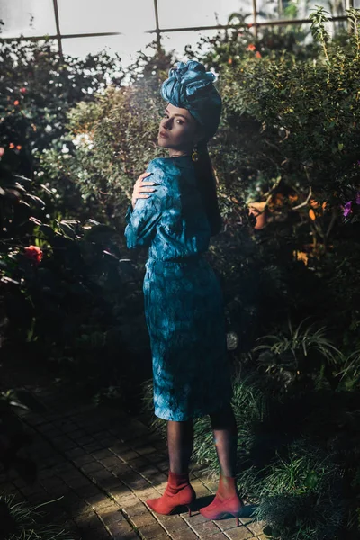 Полный обзор привлекательной женщины в голубом платье и тюрбан в оранжерее — стоковое фото