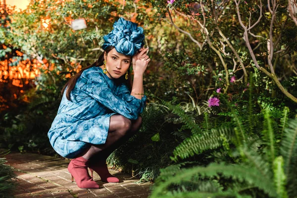 Triste donna pensierosa in abito blu e turbante seduta in giardino botanico — Foto stock