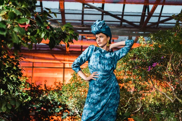 Gorgeous young woman in blue dress in turban in orangery — Stock Photo