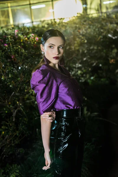 Pensive girl in purple blouse and leather pants posing in orangery — Stock Photo