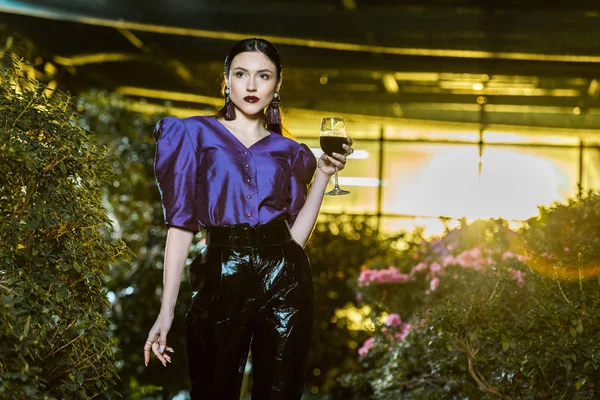 Superbe jeune femme en chemisier violet tenant verre de vin en orangerie — Photo de stock
