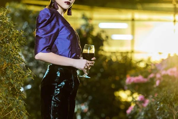 Xropped view of stunning young woman in purple blouse holding wine glass in orangery — Stock Photo