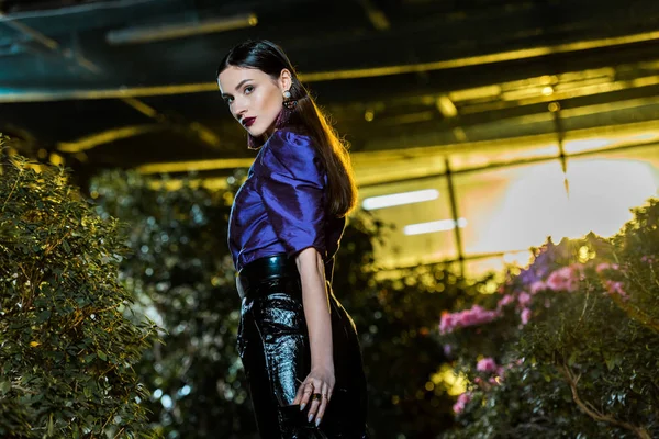 Serious young woman in purple blouse holding wine glass and looking at camera in orangery — Stock Photo