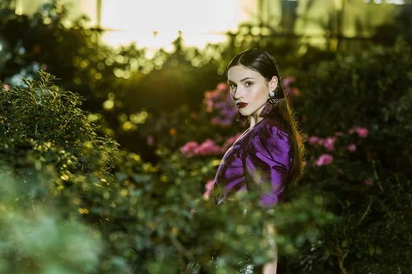 Sérieuse jeune femme en chemisier violet regardant la caméra en orangerie — Photo de stock