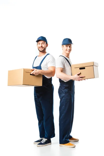 Two handsome movers looking at camera while transporting cardboard boxes on white — Stock Photo