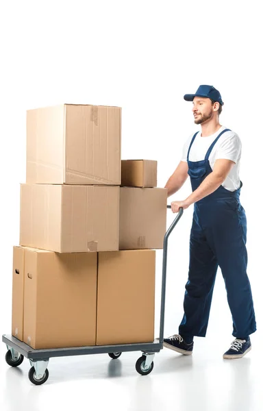 Bonito mover em uniforme transportando caixas de papelão no caminhão de mão isolado no branco — Fotografia de Stock